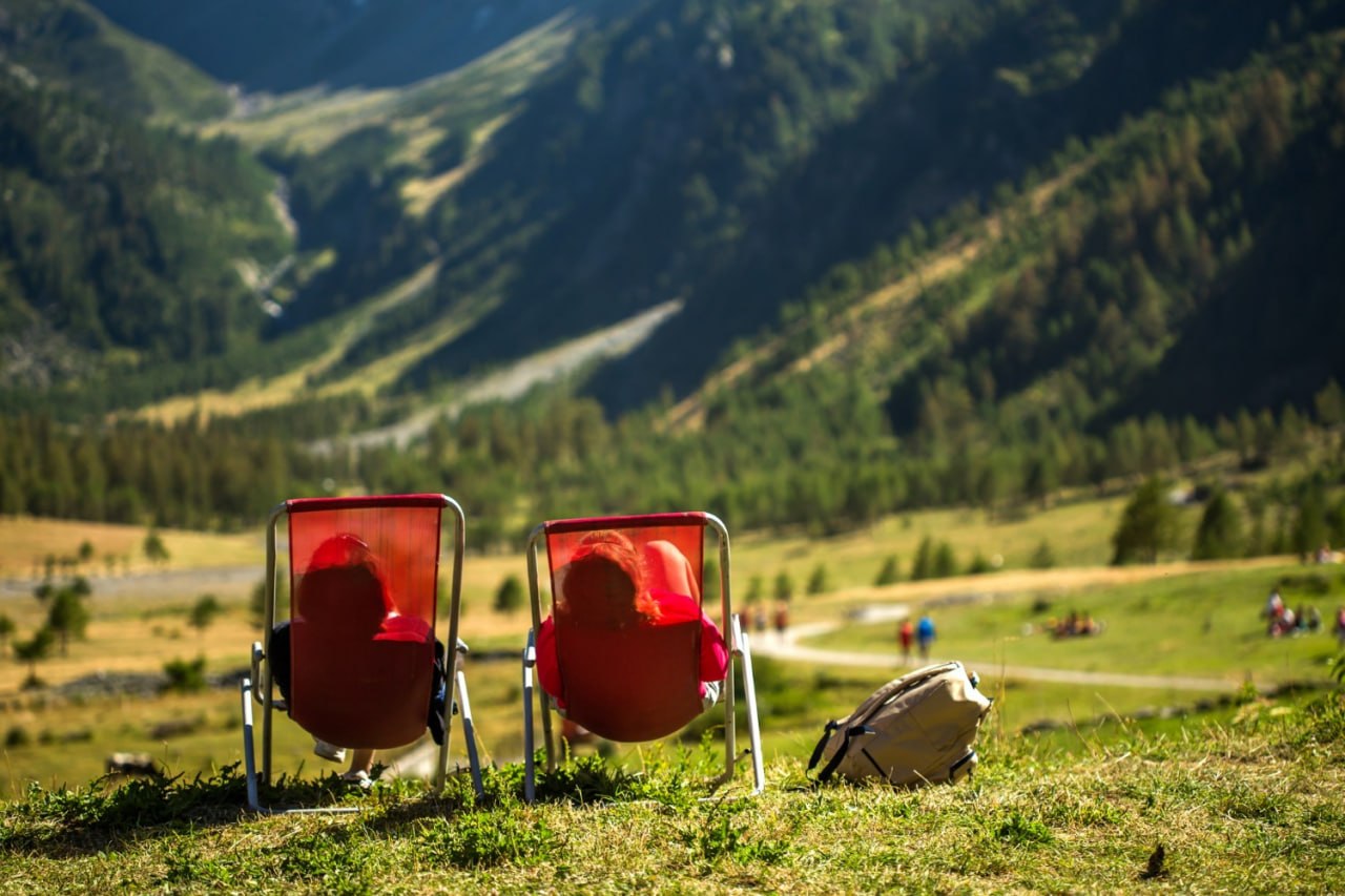 Two people relaxing in red chairs above an alpine valley