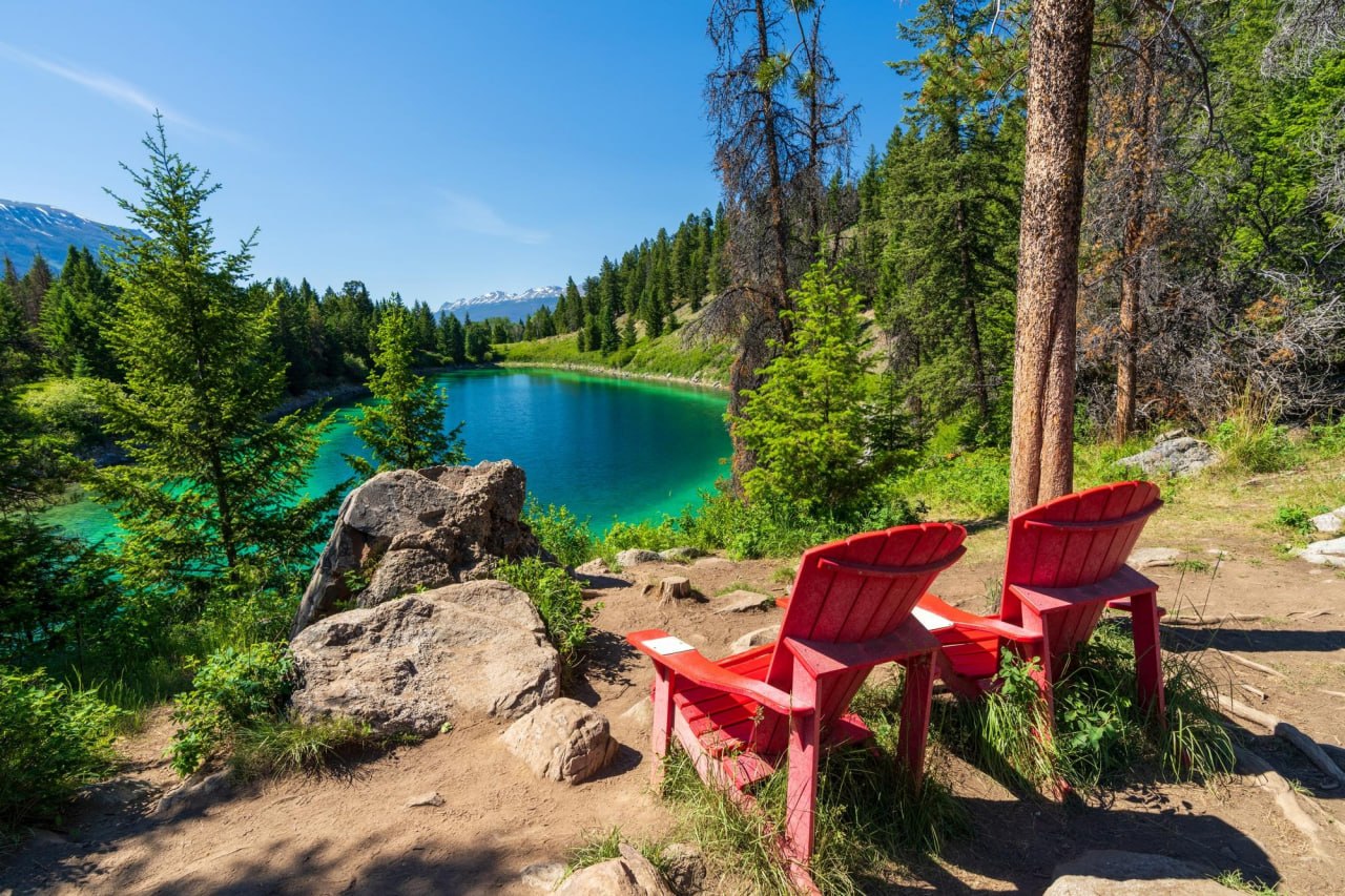 Red Adirondack chairs overlooking a turquoise mountain lake